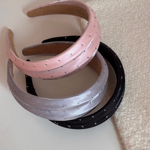 Gros plan de trois serre-têtes en satin avec strass étincelants en rose, gris et noir mat