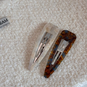 Detailed macro view of marble and tortoiseshell acetate hair clips on soft white fabric