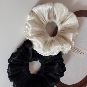 Close-up of pleated satin hair scrunchies in black and cream white with silky texture