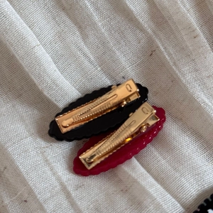 Detail view of wavy resin hair clips in black and wine red with gold metal duckbill clamps