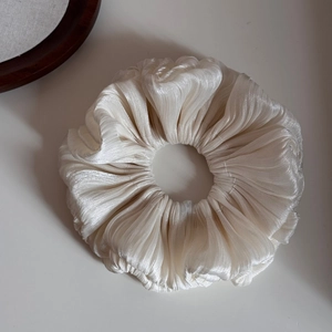 Detail of elegant pleated cream white oversized scrunchie with soft satin texture