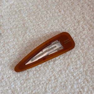 Detail of a dark brown amber-textured acetate hair clip on a soft beige fabric background