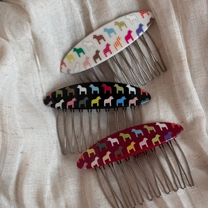 Close-up of Dala Horse hair combs in black, white and red on soft linen fabric
