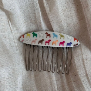 Detail of colorful Swedish Dala horse pattern on white acrylic comb with metal teeth
