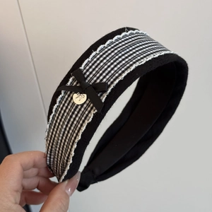 Close-up of black fabric headband with checkered ribbon, lace trim and golden bow charm