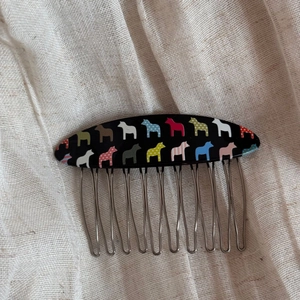 Detailed view of horse-patterned hair comb with ten metallic teeth on linen background