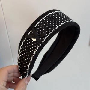 Detail of black polka dot headband with lace trim, ribbon bow and golden metal buckle