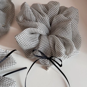 Polka dot mesh scrunchie with a black bow and heart pendant on a clean white surface