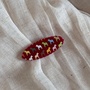 Detail of red oval hair comb featuring colorful Dala horse patterns on wavy resin edge