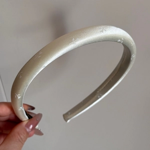 Detailstruktur des cremefarbenen Satin-Haarbands mit zarten weißen Blattmustern