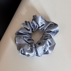 Nahaufnahme von silberblauem Satin-Haargummi mit weißem Blumendruck auf neutralem Grund