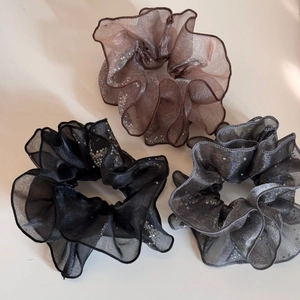 Detailed view of three sheer organza scrunchies in black, brown, and grey with silver glitters
