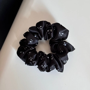 Nahaufnahme eines schwarzen Blumen-Satin-Scrunchie mit glatter Seidentextur und Falten
