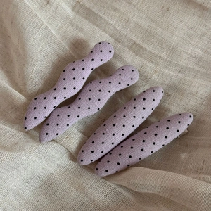 Close-up of four purple polka dot fabric hair clips on a soft linen textured surface
