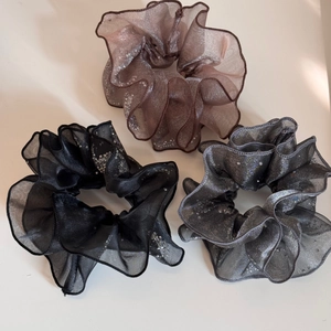 Close-up of three sparkling organza hair scrunchies in brown, black, and silver grey tones