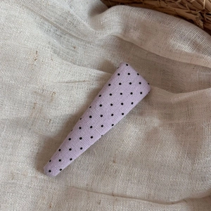 Close-up of purple polka dot fabric hair clip on a textured beige linen background