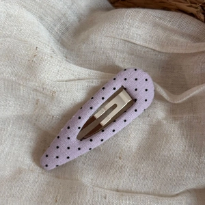 Close-up of a purple fabric BB hair clip with black polka dots on a beige background