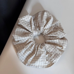 Close-up of beige and grey plaid fabric scrunchie with soft ruffled cotton texture