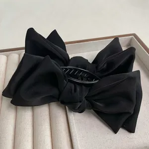 Detail of elegant black satin bow hair claw clip showing glossy fabric texture and teeth