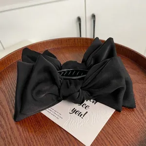 Elegant large black satin layered bow hair clip for bun styling on a wooden tray