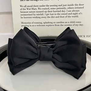 Grande pince à cheveux élégante avec double nœud en satin noir sur une assiette blanche épurée