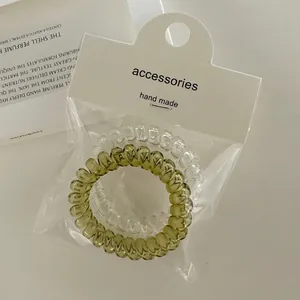 Macro shot of transparent and olive green spiral hair ties on white paper card