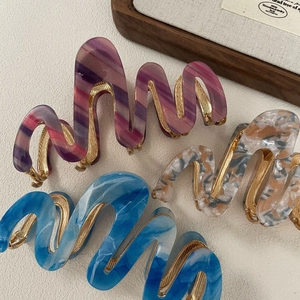 Detailopname van gegolfde haarklemmen van acetaat in paars, oranje en blauw met gouden tanden