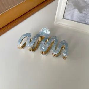 Detail van lichtblauwe marmeren acetaat haarklem met gouden metalen tanden en golvend design