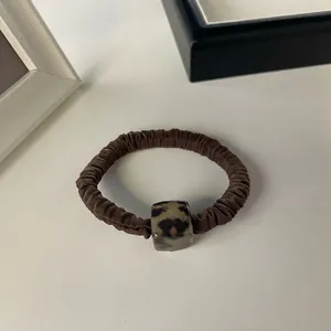 Detail of a brown pleated hair tie with a square leopard print acrylic charm