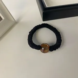 Detailed close-up of a black pleated hair tie with a smooth amber-colored decorative bead