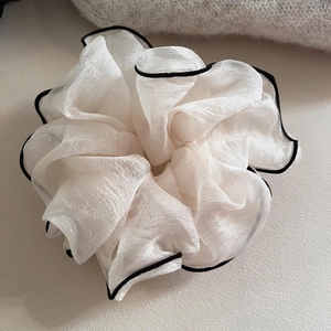 Gros plan d'un chouchou en organza blanc cassé avec d'élégants bords passepoilés noirs