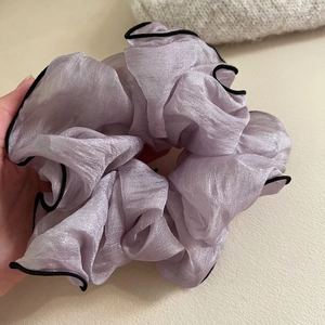 Détail d'un grand chouchou en satin violet avec bords noirs élégants et texture plissée