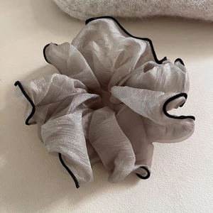 Détail du chouchou en organza champagne avec bordure noire et texture plissée douce