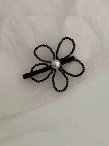 Detailed macro view of a floral hair clip with black beads and a central white pearl ornament