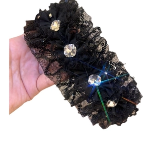 Close-up of black pleated lace headband featuring sparkling sequins and large square rhinestones