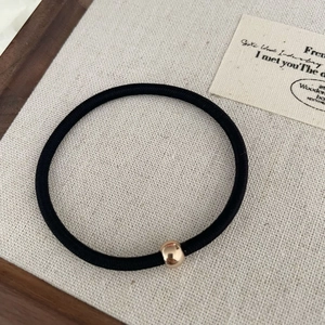 Détail d'un élastique à cheveux noir haute élasticité avec une perle en métal or rose