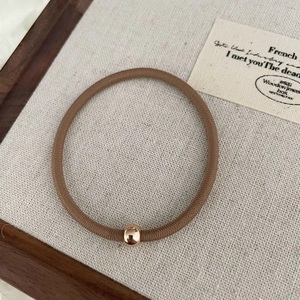 Gros plan sur un élastique à cheveux marron avec une perle dorée polie minimaliste