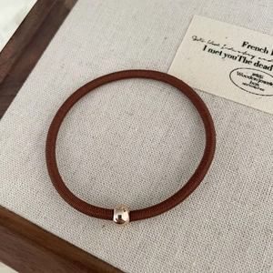 Élastique à cheveux marron avec perle dorée sur fond de tissu beige texturé
