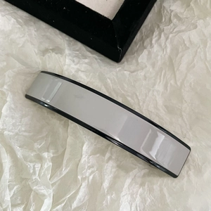 Vue détaillée d'une pince à cheveux rectangulaire en acétate gris et noir sur fond blanc