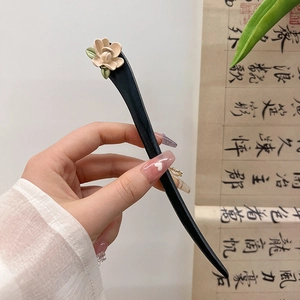 Detail of elegant black wood hairpin with white flower and delicate green leaves