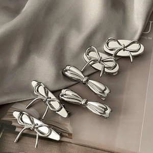 Silver metallic bow hair clips in minimalist style on a grey silk fabric background