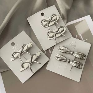 Sleek silver metal bow hair clips in three styles displayed on a minimalist card