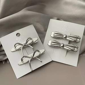 Macro shot of polished silver bow hair clips on a white card with satin background