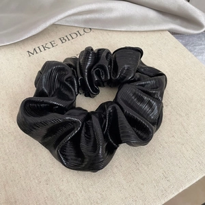 Macro detail of black pleated satin scrunchie with silk luster on beige background