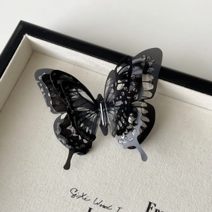 Detailed macro shot of 3D layered black butterfly hair clip with silver glitter accents
