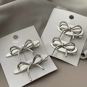 Close-up of four silver metal bow hair clips on white cardstock over grey silk fabric