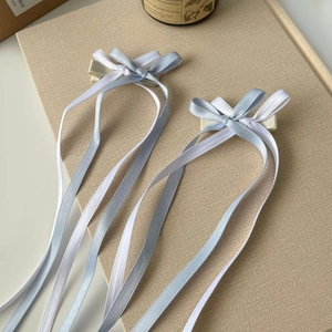 Detail of blue and white satin ribbon bow hair clips with long streamers on a beige surface