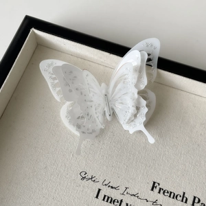 Detailed close-up of a 3D multilayer white butterfly hair clip with shimmering silver edges