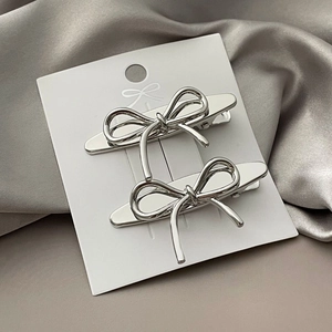 Detail of two silver metal bow hair clips on display card over grey satin fabric