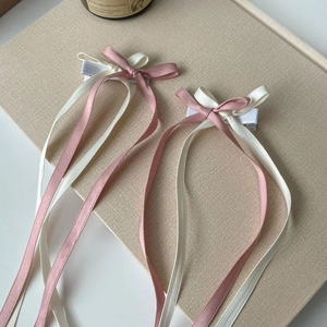 Pink and beige ballet style ribbon bow hair clips with long tassels on fabric background